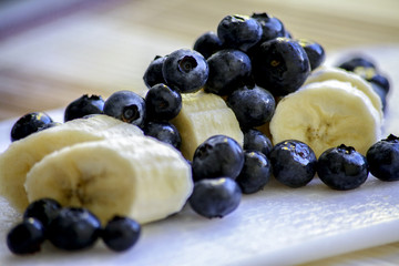 Bananas in slices and blueberries on a white board