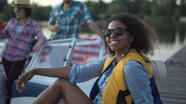 African American woman in life vest looking at camera on background of boat and people having fun.