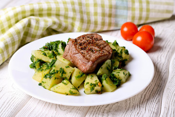 Steak with fried potatoes and spinach on wooden table