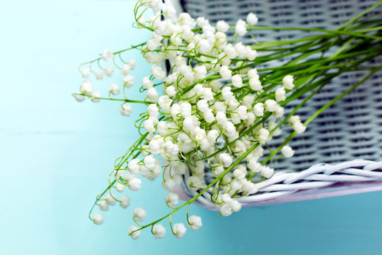 A bouquet of fresh white lilies of the valley in a wicker basket.