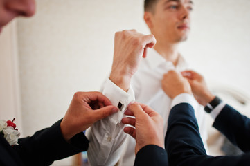 Groomsmen helping groom to dress up and get ready for his wedding in a room.