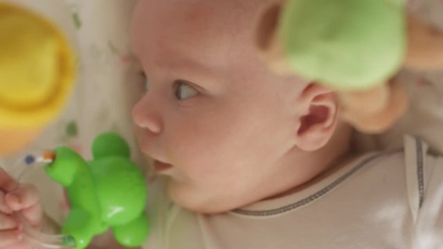 Top view shot of cute baby with soother lying in crib and looking at spinning taddy bear toys. The baby looks around and then smiles and laughs. Concept of caring for children, parental love and lack