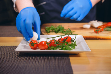Chef hands with gloves cooked. Chef  is cooking a  gourmet dish - mozzarella with basil, cherry...
