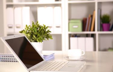 Close up view of a work desk interior with a laptop computer, a cup of coffee and white curtains on a sunny day