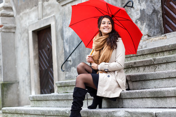 Smiling young woman with red umbrella sitting on the stairs in the old town.