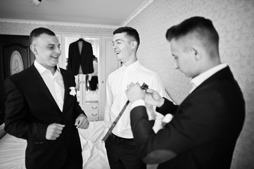 Groomsmen helping groom to dress up and get ready for his wedding in a room. Black and white photo.