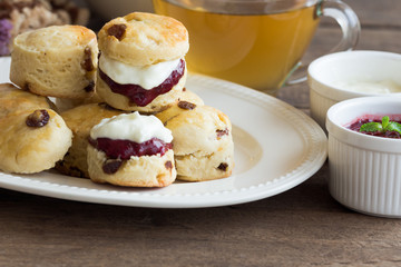 Obraz na płótnie Canvas Homemade raisin scones served with homemade strawberries jam,clotted cream and tea.Scones is English pastry for afternoon tea,cream tea. Delicious scones Devon shire or Cornish cream style. 