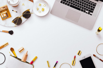 A feminine flatlay scene, featuring make up items, brushes and bags, along with a Macbook laptop...