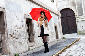 Portrait of smiling young woman with red umbrella looking at phone.