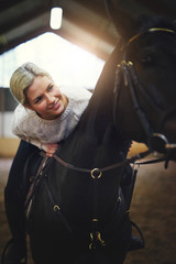 Smiling blonde female sitting astride black horse