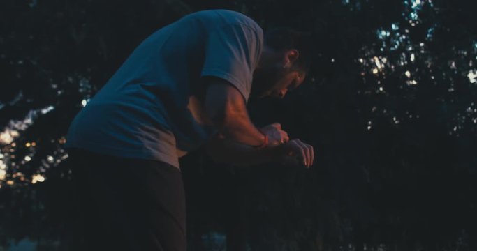 Caucasian male jogging in the park in the evening, checking progress on his smart watch. 4K UHD