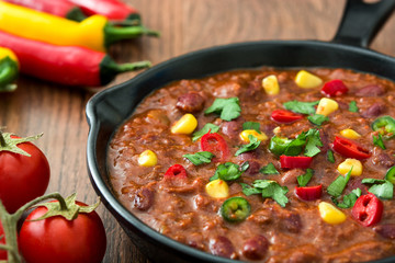 Traditional mexican tex mex chili con carne in a frying pan on wooden table
