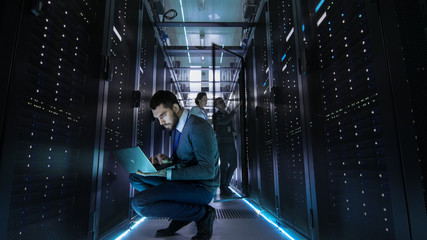 IT Technician Works on Laptop in Big Data Center full of Rack Servers.