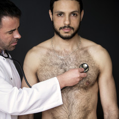 doctor with stethoscope listening to shirtless patients heartbeat
