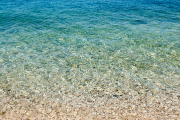 square background image of calm turquoise sea on shingle beach
