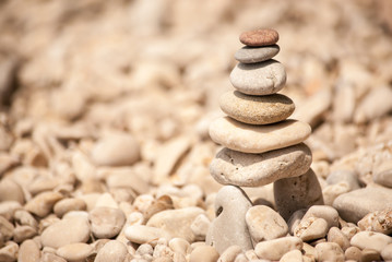 Fototapeta na wymiar Zen tower of six stones stacked on stilts on a pale pebble beach, viewed from right 