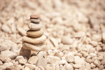 Zen tower of six stones stacked on stilts on a pale pebble beach, viewed from left
