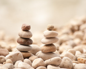 Fototapeta na wymiar Square image of two small zen pagodas of five pebbles against a blurred background of pebble beach 