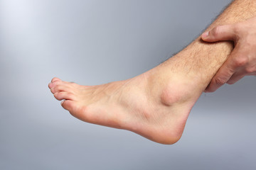 Young man suffering from pain in leg on grey background, closeup