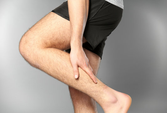 Young man suffering from pain in leg on grey background
