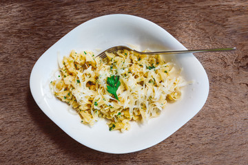 Cooked pasta campanelle sprinkled with grated cheese and greens in a white plate on a wooden table.