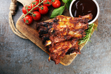 Spicy hot grilled spare ribs from a summer BBQ served with fresh tomatoes on an old vintage wooden cutting board