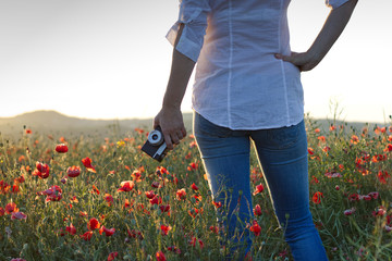 Fototapeta na wymiar Old retro camera in a womans hand standing in a blooming poppy field. 