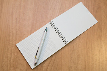 A notebook and ballpoint pen lying on a wooden table.