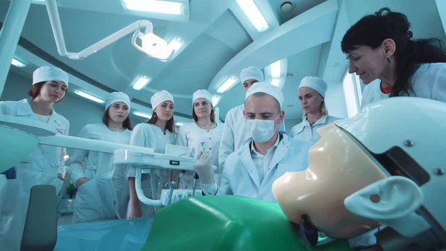 Dentist giving a demonstration to a group of young students in a medical school or university using a dummy to show the technique