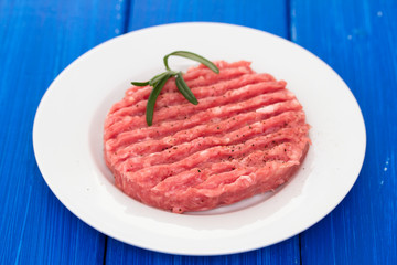 raw hamburger on white plate on wooden background