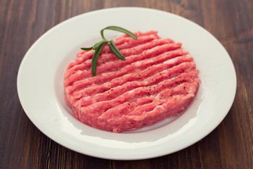 raw hamburger on white plate on wooden background