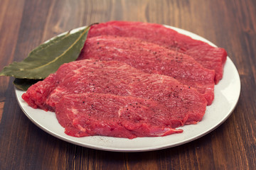 raw meat on white plate on wooden background