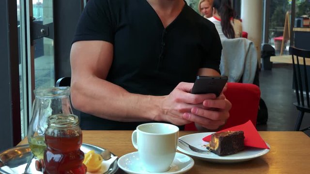 A young handsome man sits at a table in a cafe and takes pictures of his meal - closeup