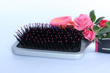 Une brosse à cheveux  accompagnée de roses rose décorative et d'élastique sur fond blanc - obrazy, fototapety, plakaty