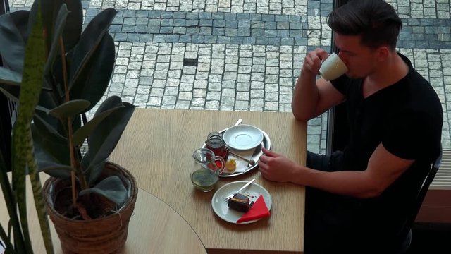 A young handsome man sits at a table in a cafe and drinks tea - top view