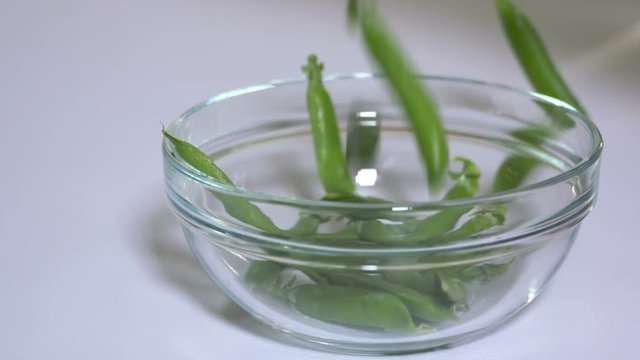 Closeup of freshly picked pea pods falling into a glass bowl in slow motion