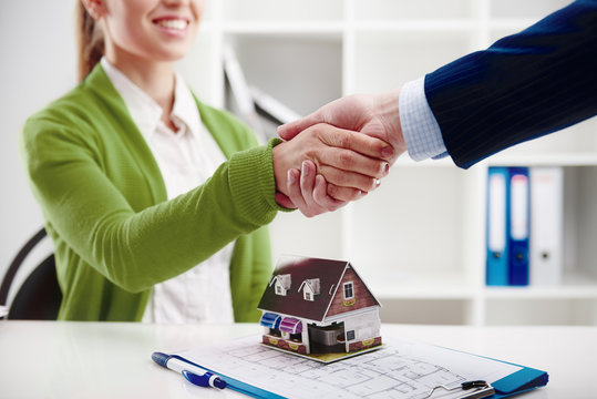 Woman agent shaking hands with new apartment owner over house model at the desk. 