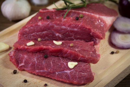 Raw beef steak on wooden table with rosemary, garlic and peppercorn
