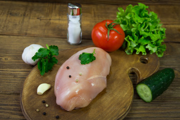 Raw chicken breasts on cutting board with parsley, garlic and peppercorn