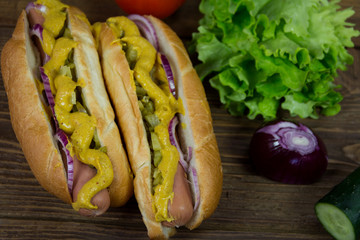 Hot dog with onion, mustard and pickles on wooden background