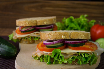 Sandwich with ham, cheese, tomatoes, lettuce, cucumbers and onions on a wooden background