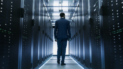 Fototapeta na wymiar Following Shot of IT Engineer Walking Through Data Center with Rows of Working Rack Servers on Both Sides.