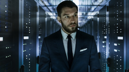 Businessman Walking Through Data Center Corridor  with Server Rack Visually Inspecting Working Server Cabinets.