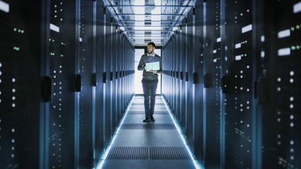 IT Technician Works on Laptop in Big Data Center full of Rack Servers. He Runs Diagnostics and...