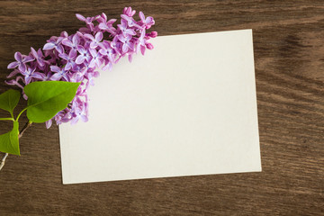 Purple lilac flowers with blank greeting card on the wooden table.