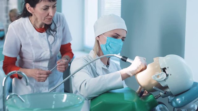 Dentistry student or hygienist practicing on a dummy at a medical school as a qualified teacher demonstrates the technique to her from behind