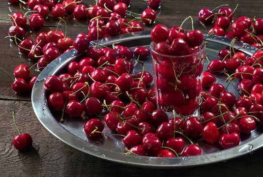 A lot of cherries on the table, on a tray and in a glass