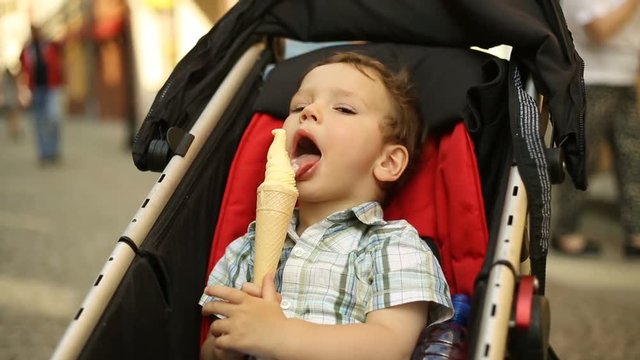 Cute, little child sitting in the pushchair and eating tasty ice cream
