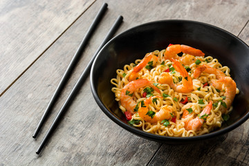 Noodles and shrimps with vegetables in black bowl on wooden table
