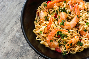 Noodles and shrimps with vegetables in black bowl on wooden table
